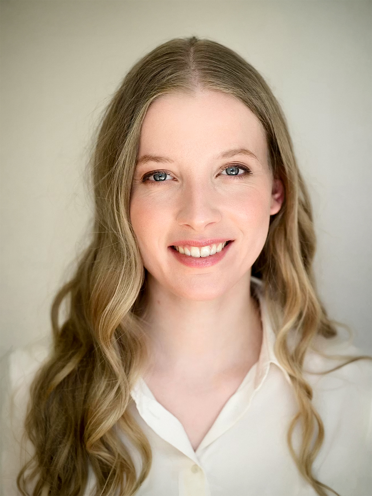 Cindy Klink in einer weißen Bluse vor einer unscharfen, beigen Wand.