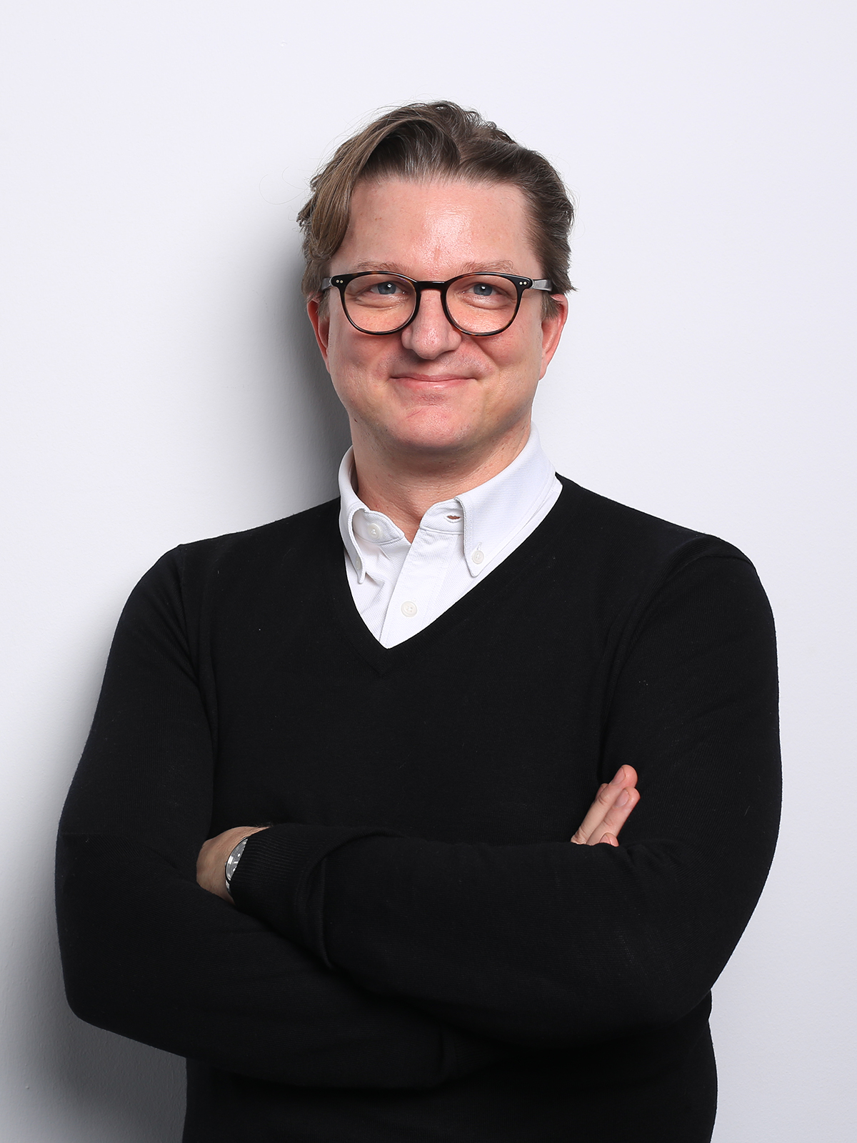 Torsten Anstädt steht mit verschränkten Armen vor weißem Hintergrund und trägt ein weißes Hemd unter einem schwarzen Pullover